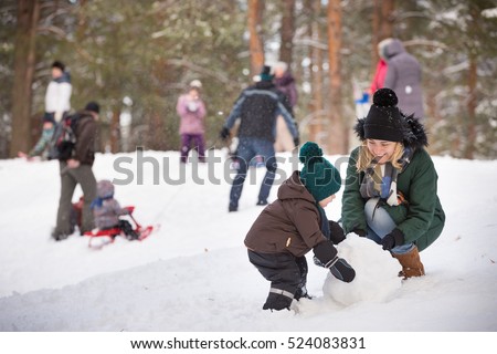 Cute little toddler boy and his mother playing with snow and making snowman. Child having fun outdoors in winter.