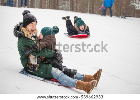 Mother and little toddler boy sliding down the hill in the winter forest and having fun with snow. Family enjoying winter. Child and woman outdoors. Winter, Christmas and lifestyle concept.