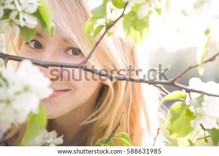 Portrait of beautiful young woman in apple trees blooming park on a sunny day. Smiling girl with apple trees flowers. Happy girl. Happiness concept.