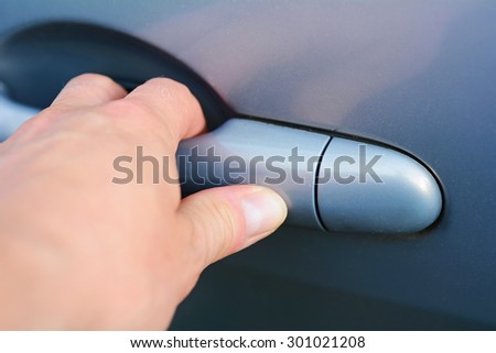 Mans hand holding the handle and opening blue car door.