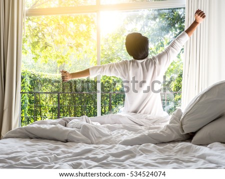 lazy man waking up in the bed rising hands to window in the morning with fresh feeling relax