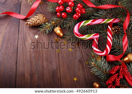 Christmas arrangement of branches of trees, candy in red strip, golden acorns, tinsel, decorative red berries on a dark wooden background.
