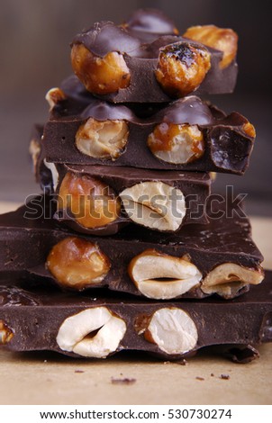 Dark chocolate with hazelnuts and caramel on parchment paper on a dark wooden background.