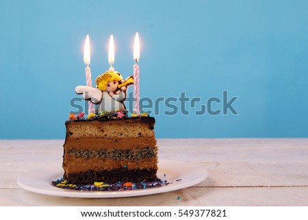 Children's birthday cake decorated with marzipan angel and candles on a white wooden table on a blue background.