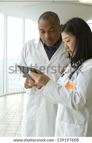 Female Asian doctor with African American doctor looking over charts on tablet