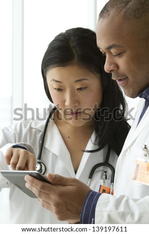 Female Asian doctor with African American doctor looking over charts on tablet