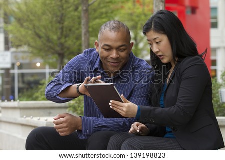 Asian business woman and African business man on their lunch break looking at their Tablet