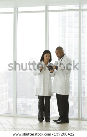 Wide shot of Asian female doctor and African American doctor looking over charts on tablet