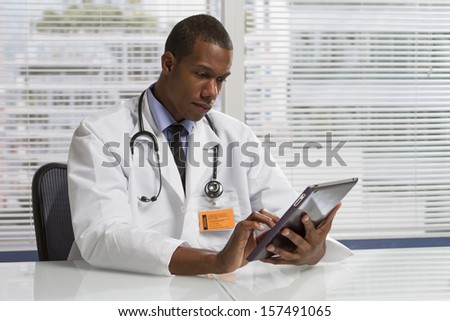 Black doctor at desk with electronic tablet, horizontal