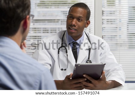 Black doctor with patient and using electronic tablet, horizontal