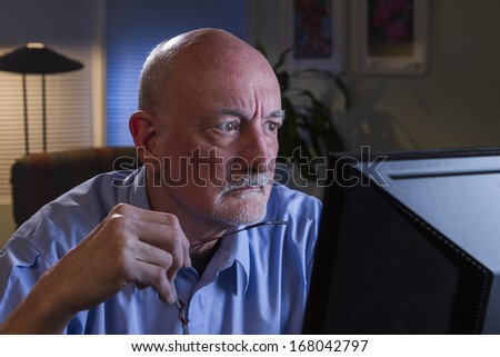 Older man studying computer and taking off glasses, horizontal