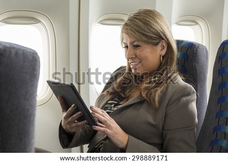 Hispanic business woman on airplane using tablet device,