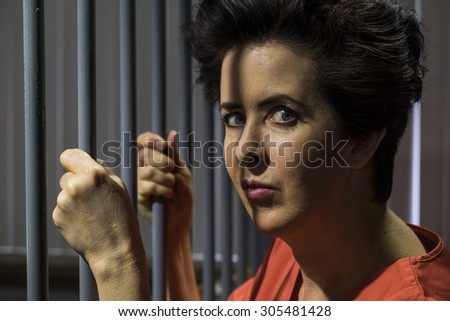 Caucasian female behind bars in a jail cell