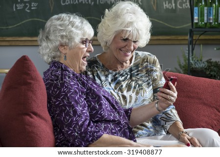 Two senior women sitting on a couch looking at a cell phone