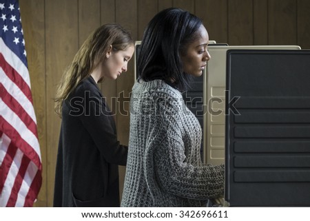 Two young adult women voting in a voting booth
