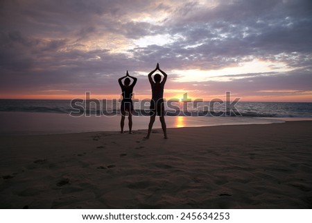 Two people doing yoga at sunset