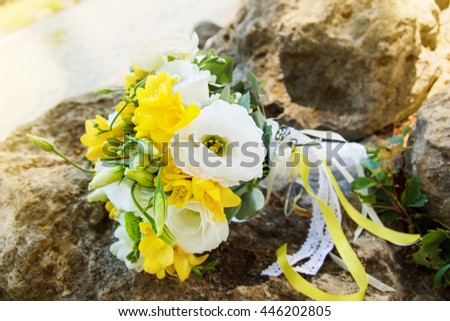 wedding concept. wedding flowers on the rocks on the beach. bouquet with yellow flowers, freesia, eustoma, lace, tape, ribbon, band, strip, sash, fillet