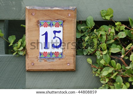 tiled number fifteen sign for home against green fence with vegetation