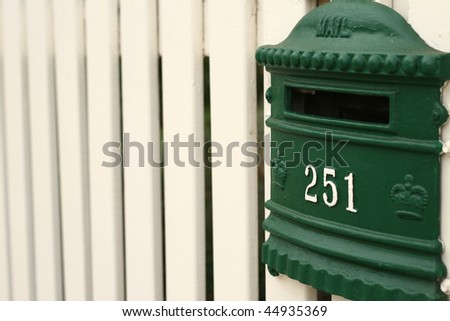 green mailbox on cream white picket fence