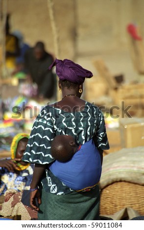DJENNE, MALI - JANUARY 16, 2006: Local woman carries her child in the market on January 16, 2006, Djenne, Mali. Every Monday there is a huge and colorful market in town.