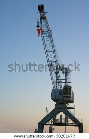 A crane with a red hook in Husum at the harbour. In the background you can see a clear blue sky.