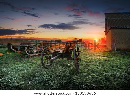 Sunrise on the farm. Spring frosts. Frost on the grass. Old wooden wagon and sleigh in the bright light of sunrise.