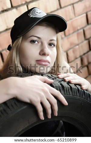 Sexy blonde with a car tire on the background of a brick wall.