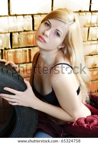Sexy blonde with a car tire on the background of a brick wall.
