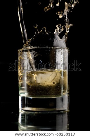 Glass of whiskey on a black background. Whiskey splash in a glass. Whiskey with ice.