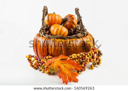 A fall harvest basket filled with pumpkins and pine cones against a white background.