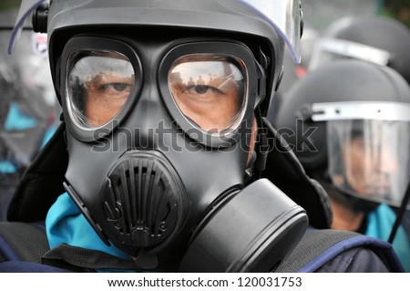 BANGKOK - NOV 24: A riot police officer wears a gas mask at anti-government rally at Makhawan Bridge on Nov 24, 2012 in Bangkok, Thailand. Police fired tear gas to deter protesters.