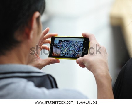 BANGKOK - JUN 30: A passerby uses a smartphone to capture an anti-government rally on Jun 30, 2013 in Bangkok, Thailand. The protesters known as V for Thailand call for the government to be removed.