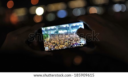 BANGKOK - DEC 22: A passerby uses a smartphone to capture a large anti government rally at Victory Monument in the city centre on Dec 22, 2013 in Bangkok, Thailand.