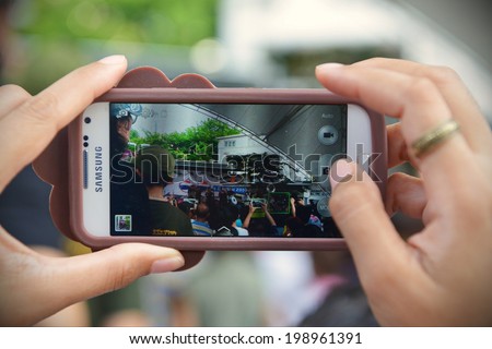 BANGKOK - JUN 4: A passerby uses a smartphone to capture an army organised pro-military event titled \'Return Happiness to Thailand\' following Thailand\'s army coup on Jun 4, 2014 in Bangkok, Thailand.