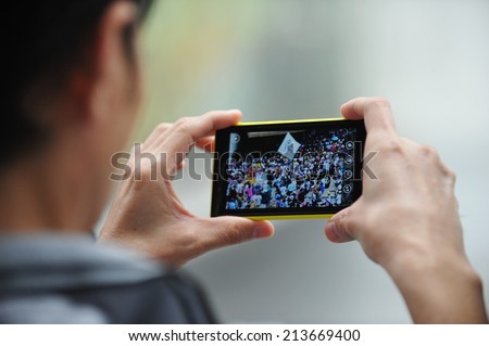 BANGKOK - JUNE 30: A passerby uses a smartphone to capture an anti government rally on June 30, 2013 in Bangkok, Thailand. The protesters call for political reform and the government to be overthrown.