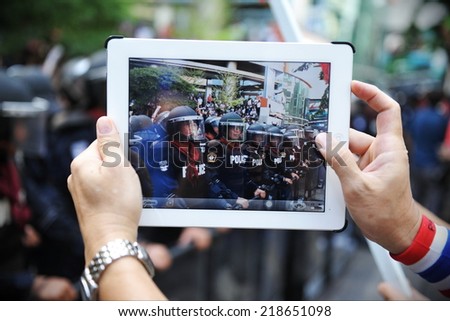 BANGKOK - NOV 29: An anti-government protesters uses a tablet device to capture a police line at a large rally outside the ruling Pheu Thai party\'s headquarters on Nov 29, 2013 in Bangkok, Thailand.