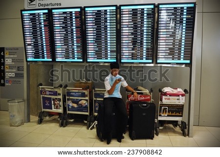 BANGKOK - JUL 6: A traveler waits on luggage under departures board at Suvarnabhumi International Airport on Jul 6, 2012 in Bangkok, Thailand. The airport handles 45 million passengers a year.