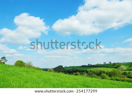 Scenic View of a Green Farmland Field with a Beautiful Blue Cloudy Sky above in Wiltshire England