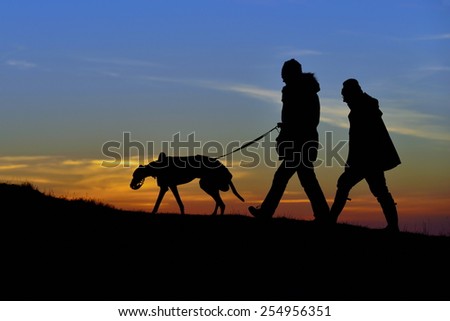 Silhouetted View of People Walking a Dog on a Hill against a Sky at Sunset