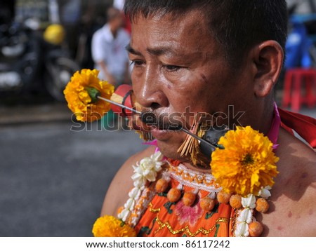 PHUKET - OCT 4: A Taoist spirit medium with his cheeks pierced with Chinese God idol skewers participates in a procession marking the Phuket Vegetarian Festival on Oct 4, 2011 in Phuket, Thailand.