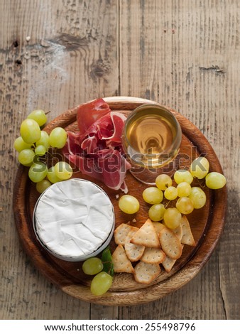 Camembert (brie) cheese on cutting board with wine, grape, Prosciutto and crackers, selective focus