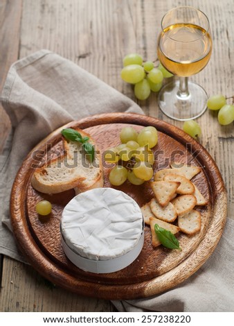 Camembert (brie) cheese on cutting board with wine, grape, Prosciutto and crackers, selective focus