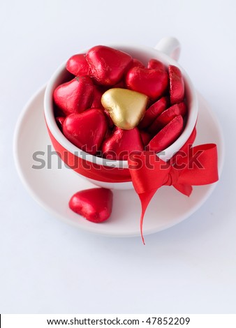White cup with saucer with red and gold chocolate hearts and red ribbon. Photo on a white background