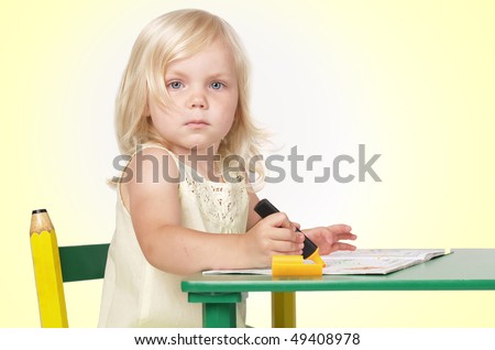 The girl sits at a table and paints the book a felt-tip pen