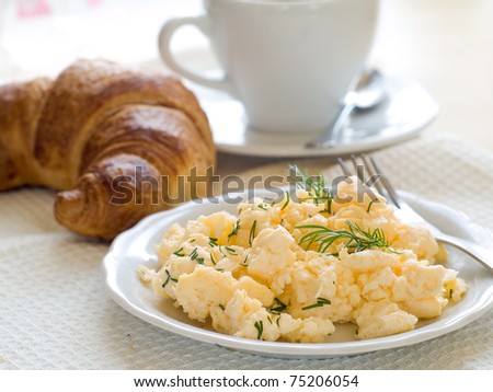 A plate of creamy scrambled eggs garnished with dill, a cup of coffee with milk