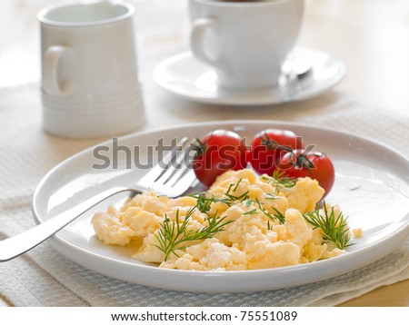 A plate of creamy scrambled eggs garnished with dill, a cup of coffee