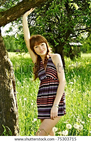 portrait of a young pretty woman posing next to a tree on a meadow during spring time