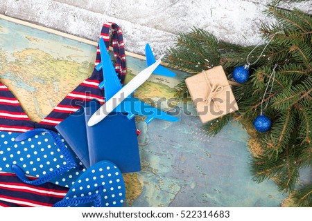 Christmas concept - travel. Fir branches with snow, maps, swimsuit, passports, gift box, flops and toy airplane