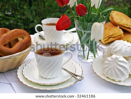 The table set for afternoon tea in a summer garden - white tea-things, pastry, marshmallows, flowers in a vase, blur background
