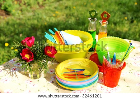 A table with bright multicolor summer picnic plastic accessories, plates and dishes, napkins, bottles and flowers